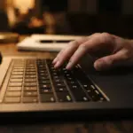 A close-up, low-angle shot of a laptop keyboard, softly lit by a focused, warm desk lamp at night